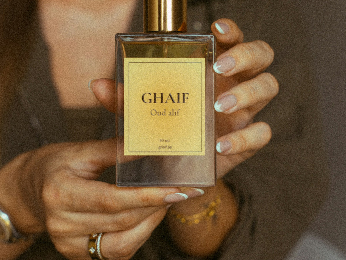 Ajmal perfumes — hands holding a warm amber oud eau de parfum bottle